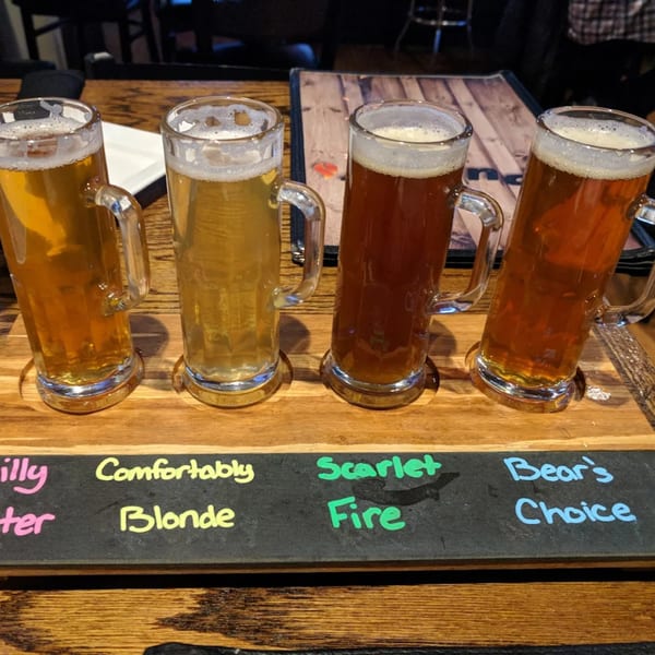 Four beer mugs with different colored beers on a wooden tray with labels at Pub 47.