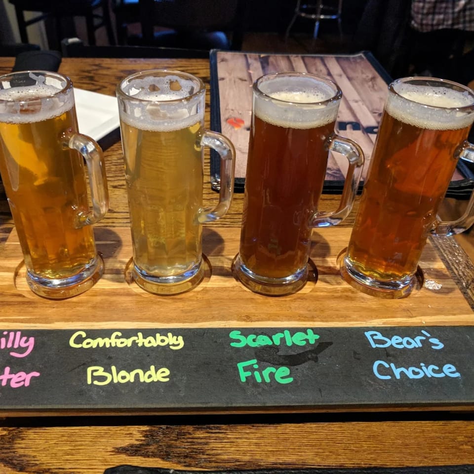 Four beer mugs with different colored beers on a wooden tray with labels at Pub 47.