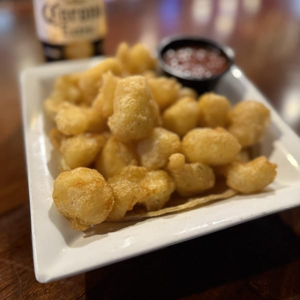 A white rectangular plate filled with golden-brown fried cheese curds and a side of red dipping sauce.