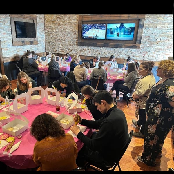 People decorating cookies at tables with pink tablecloths inside Pub 47, with TVs on the brick wall.