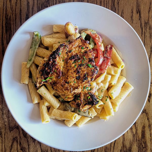 Grilled chicken with rigatoni pasta, red peppers, and green beans in a creamy sauce.