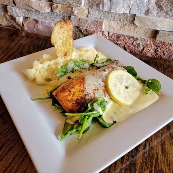 Seared salmon with creamy sauce, lemon, spinach, mashed potatoes, and a potato chip.