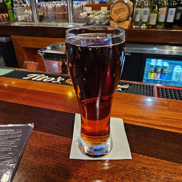 A tall glass of amber beer sits on a white napkin on a wooden bar top at Pub 47.