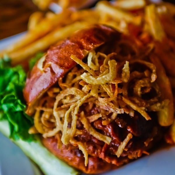 Close-up of a Pub 47 BBQ pulled pork sandwich topped with crispy fried onions and a side of fries.