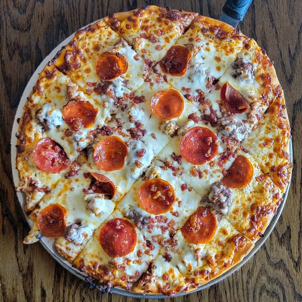 Overhead view of a Pub 47 pepperoni, sausage, and bacon pizza on a wooden table.